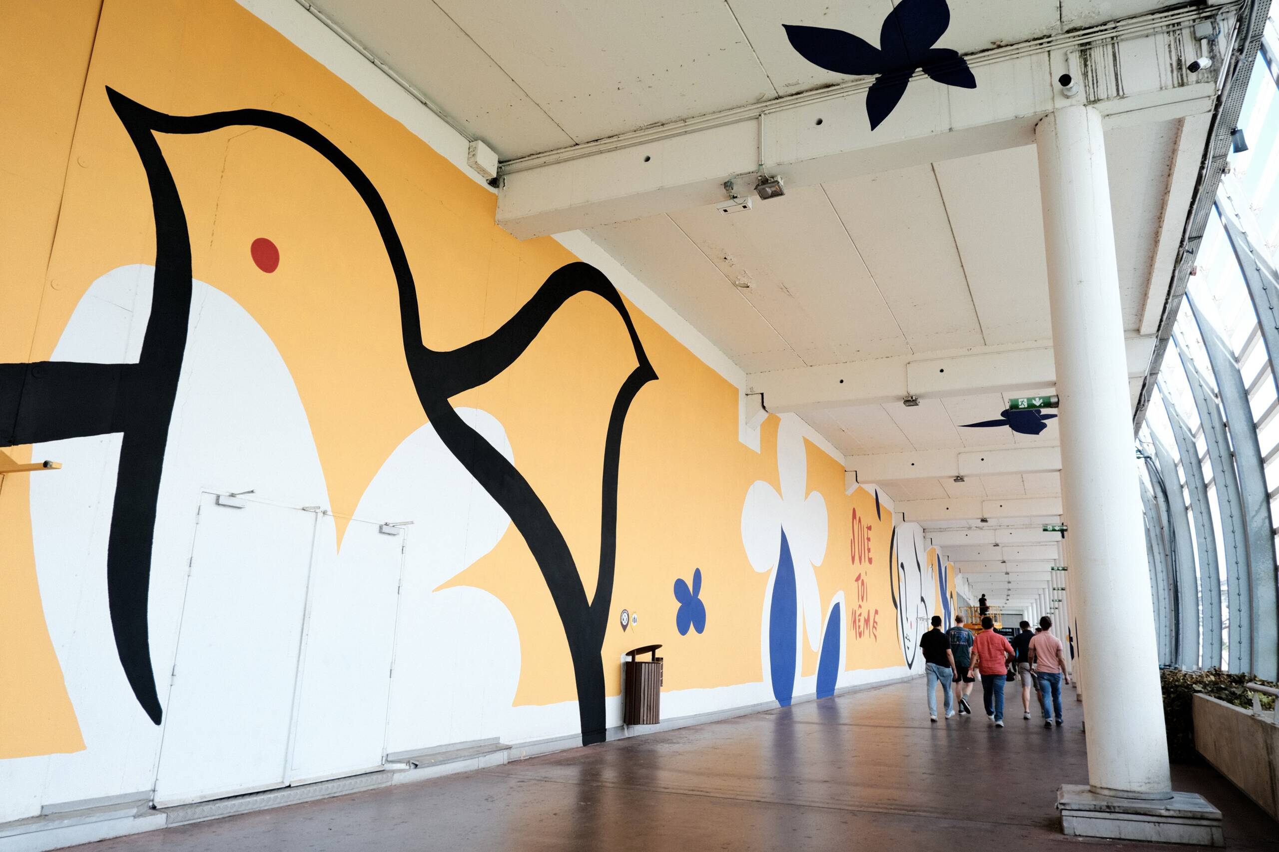 Fresque extérieure au Carré de Soie à Vaulx-en-Velin. Fond jaune, avec oiseaux noirs, et fleurs bleues.